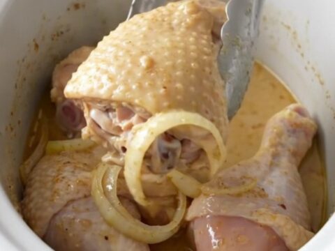 Slow cooked chicken leg quarters smothered in a thick, creamy white gravy on a white plate.