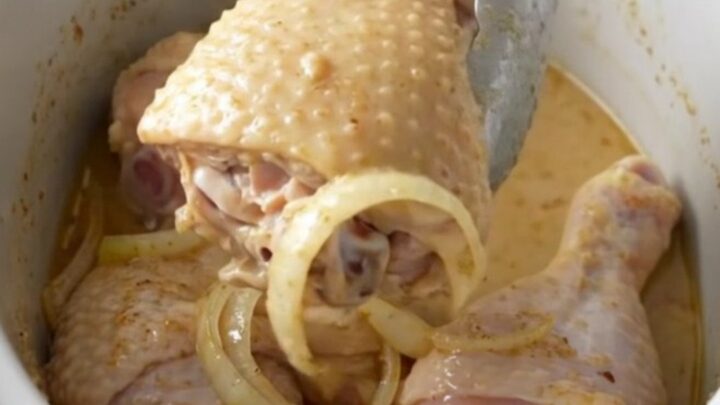Slow cooked chicken leg quarters smothered in a thick, creamy white gravy on a white plate.
