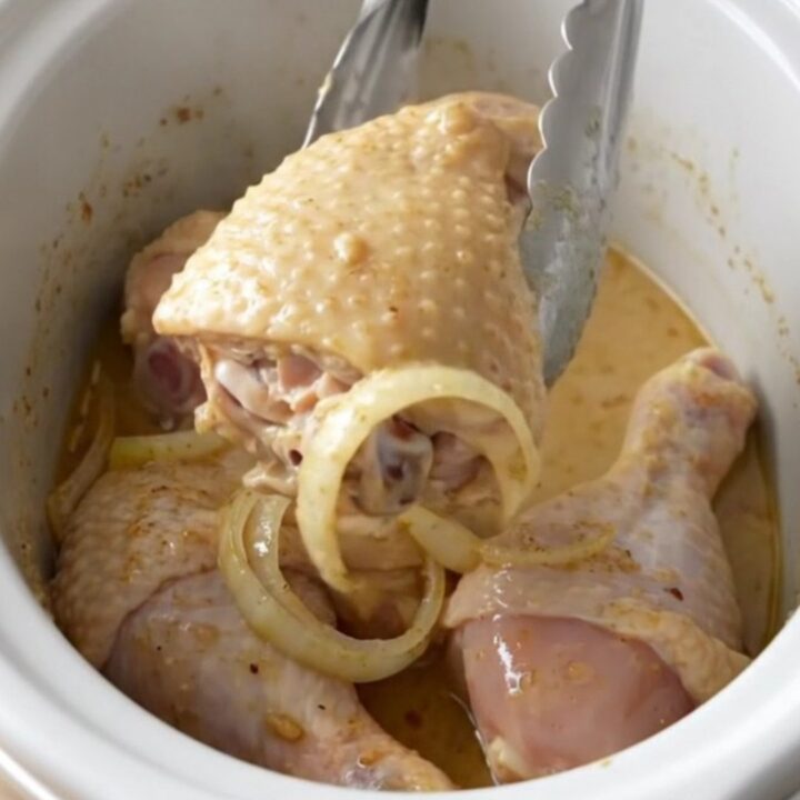 Slow cooked chicken leg quarters smothered in a thick, creamy white gravy on a white plate.