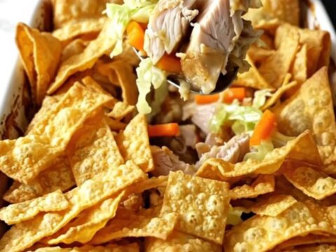 A golden, bubbling chicken egg roll casserole in a white ceramic dish, topped with crispy wonton strips.