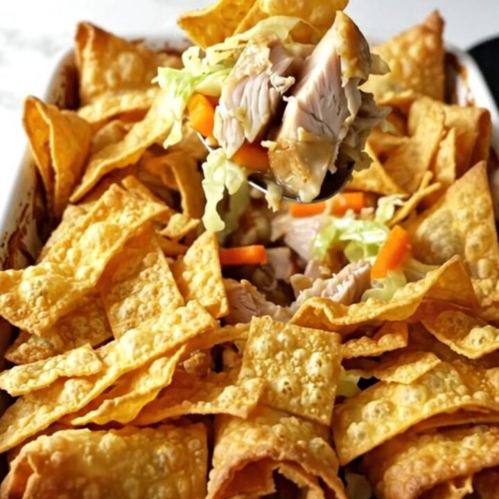A golden, bubbling chicken egg roll casserole in a white ceramic dish, topped with crispy wonton strips.