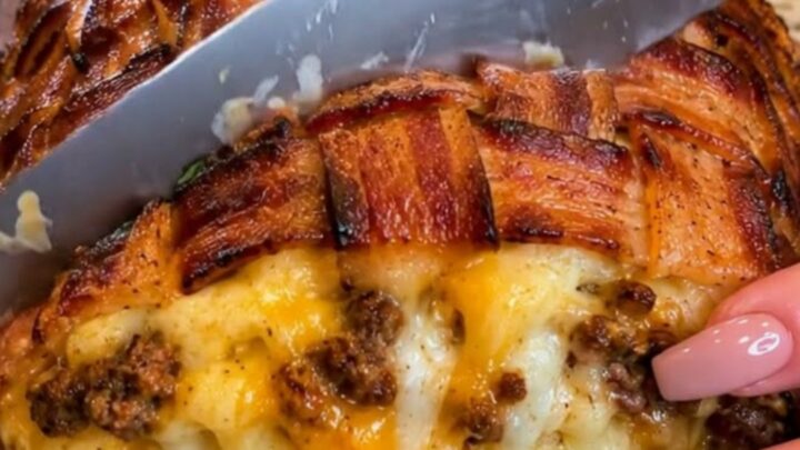 A sliced bacon-wrapped meatloaf on a wooden board showing melted cheddar cheese oozing from the center.