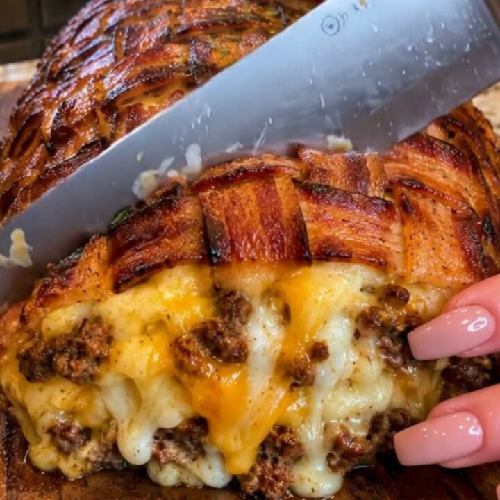 A sliced bacon-wrapped meatloaf on a wooden board showing melted cheddar cheese oozing from the center.