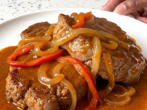 A close-up shot of tender pork Swiss steak in a slow cooker with peppers and onions.