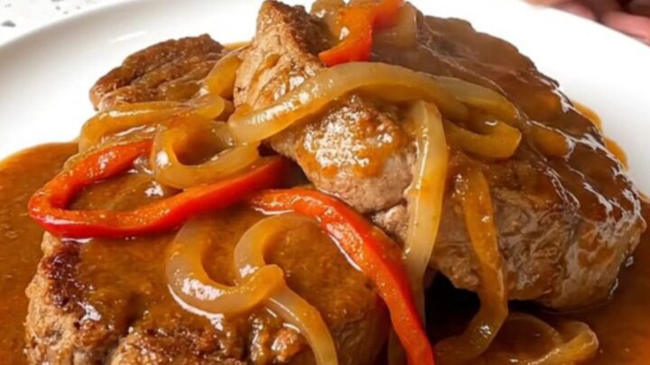 A close-up shot of tender pork Swiss steak in a slow cooker with peppers and onions.