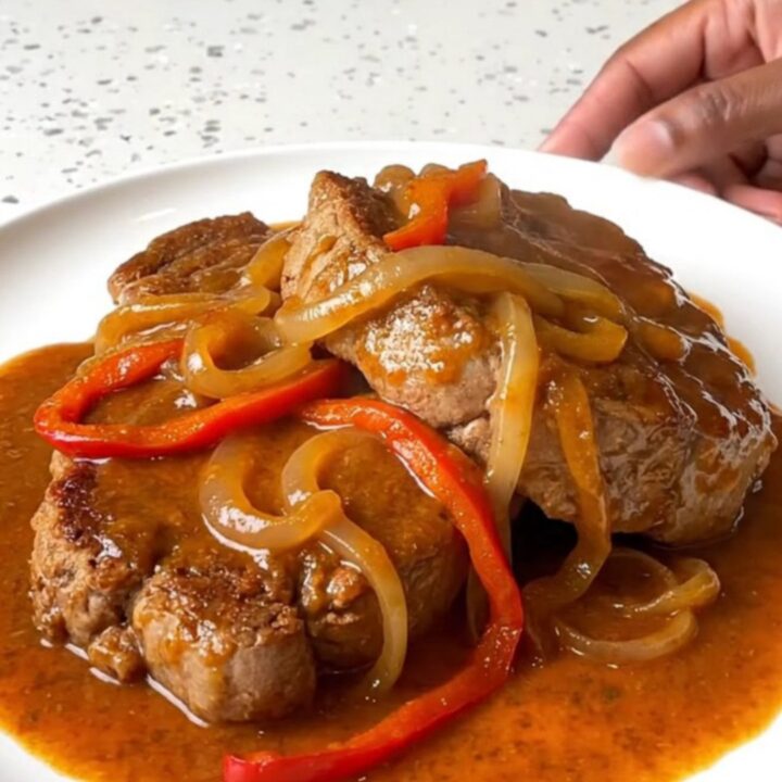 A close-up shot of tender pork Swiss steak in a slow cooker with peppers and onions.