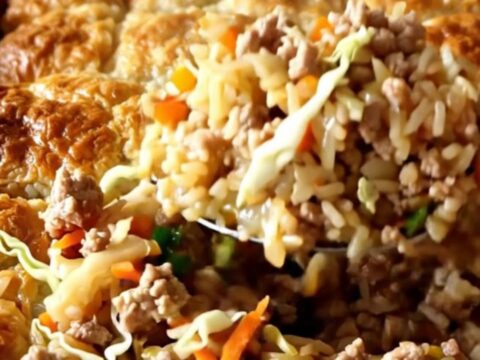 A golden, bubbling baked rice dish with ground pork and shredded cabbage in a white ceramic pan.