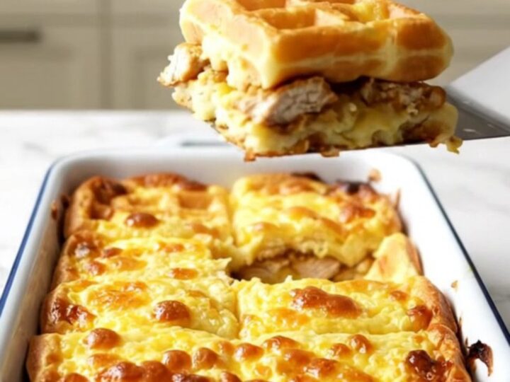A rectangular baking dish filled with golden baked waffles and crispy breaded chicken bites.