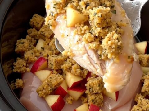 A close-up view of the slow cooker filled with chicken breasts topped with herb stuffing and diced apples.