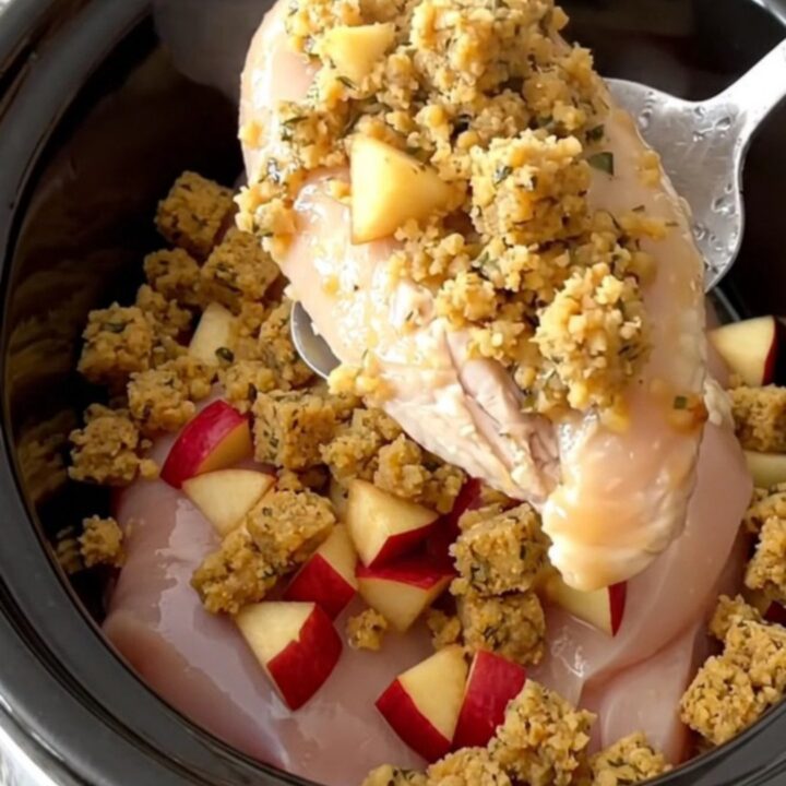 A close-up view of the slow cooker filled with chicken breasts topped with herb stuffing and diced apples.