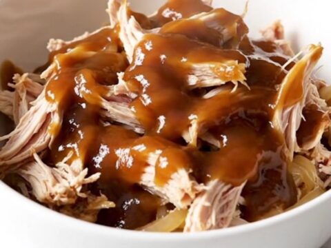 A close-up of tender, shredded pulled chicken in a sweet tea barbecue sauce with soft onions in a white bowl.