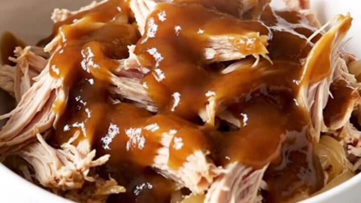 A close-up of tender, shredded pulled chicken in a sweet tea barbecue sauce with soft onions in a white bowl.