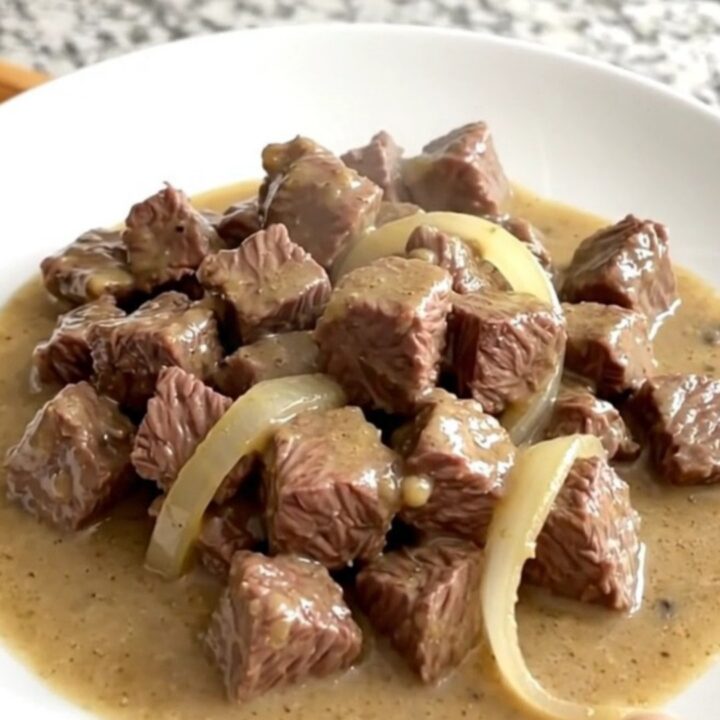 A close-up of tender beef tips in a creamy mushroom gravy served on a white plate.