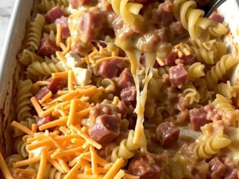 A ceramic baking dish filled with rotini pasta, sausage, and a rich tomato sauce topped with melted cream cheese and cheddar.