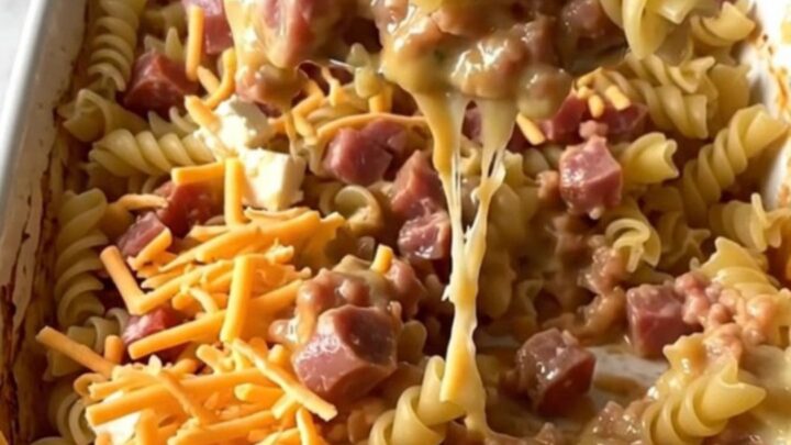 A ceramic baking dish filled with rotini pasta, sausage, and a rich tomato sauce topped with melted cream cheese and cheddar.
