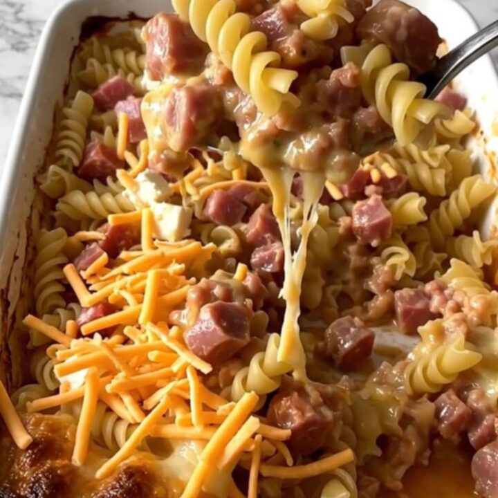 A ceramic baking dish filled with rotini pasta, sausage, and a rich tomato sauce topped with melted cream cheese and cheddar.