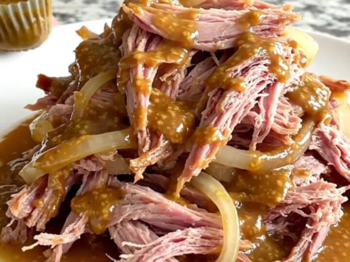 A close-up of tender, shredded brown sugar Dijon pulled ham on a white plate.