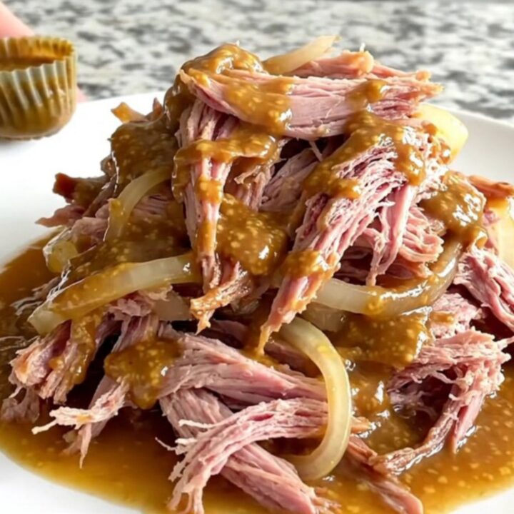 A close-up of tender, shredded brown sugar Dijon pulled ham on a white plate.
