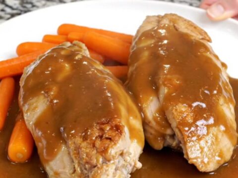 Slow cooked chicken breasts and baby carrots in a glossy brown sugar butter sauce on a white plate.