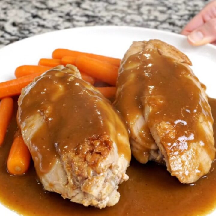 Slow cooked chicken breasts and baby carrots in a glossy brown sugar butter sauce on a white plate.