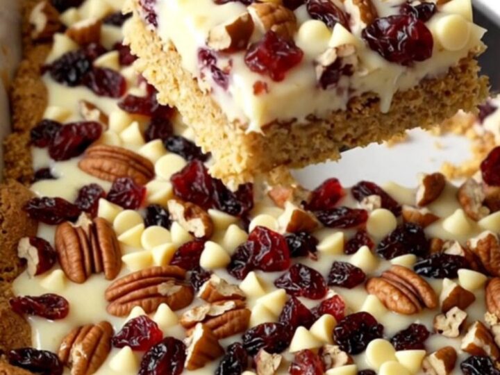 A top-down view of white chocolate cranberry magic bars in a white ceramic baking dish on a speckled counter.