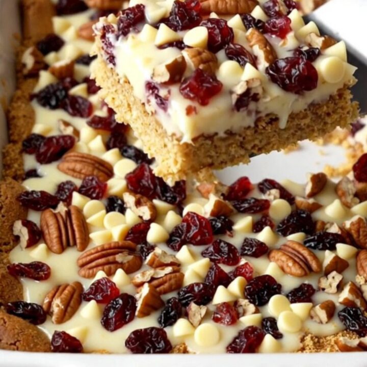 A top-down view of white chocolate cranberry magic bars in a white ceramic baking dish on a speckled counter.
