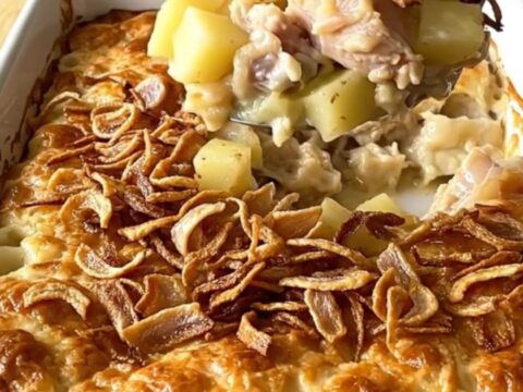 A top-down view of a creamy chicken and potato bake in a white ceramic dish topped with crispy fried onions.
