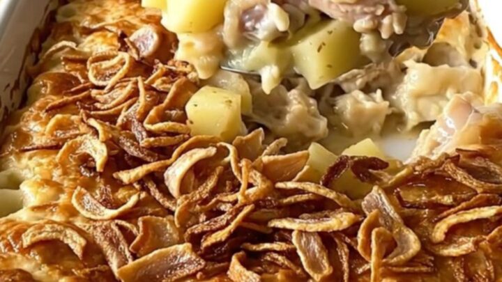 A top-down view of a creamy chicken and potato bake in a white ceramic dish topped with crispy fried onions.