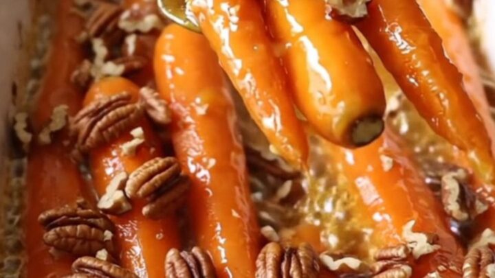 A ceramic baking dish filled with roasted carrots glazed in maple Dijon butter and topped with pecans.