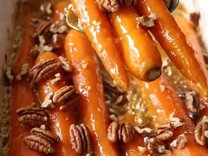 A ceramic baking dish filled with roasted carrots glazed in maple Dijon butter and topped with pecans.