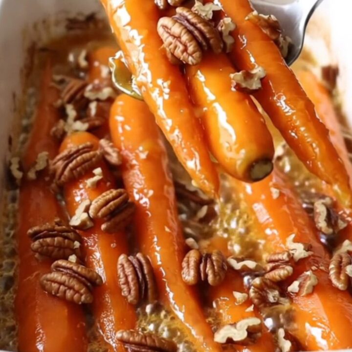 A ceramic baking dish filled with roasted carrots glazed in maple Dijon butter and topped with pecans.