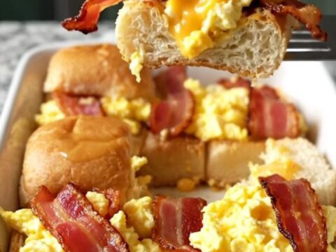 A top-down view of a rectangular baking dish filled with golden brown bacon, egg and cheese sliders.