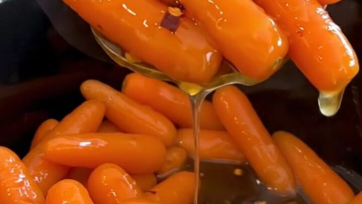 A top-down view of cooked baby carrots in a black slow cooker, glazed with a shiny honey butter sauce.