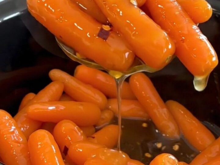 A top-down view of cooked baby carrots in a black slow cooker, glazed with a shiny honey butter sauce.