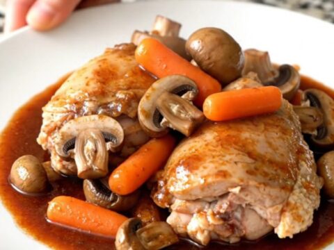 A rustic bowl of slow-cooked coq au vin featuring tender chicken thighs, mushrooms, and carrots in a rich red wine sauce.
