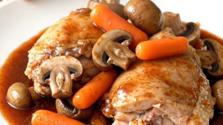 A rustic bowl of slow-cooked coq au vin featuring tender chicken thighs, mushrooms, and carrots in a rich red wine sauce.