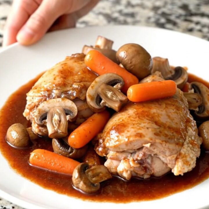 A rustic bowl of slow-cooked coq au vin featuring tender chicken thighs, mushrooms, and carrots in a rich red wine sauce.