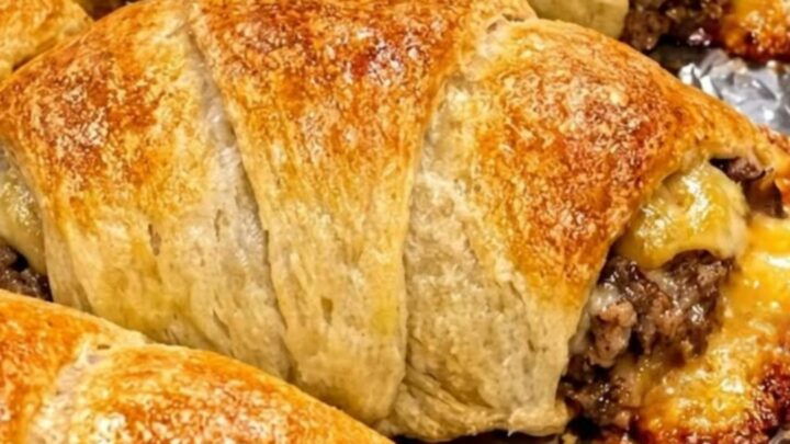 A row of golden-brown cheesy beef crescent rolls arranged on crinkled aluminum foil.