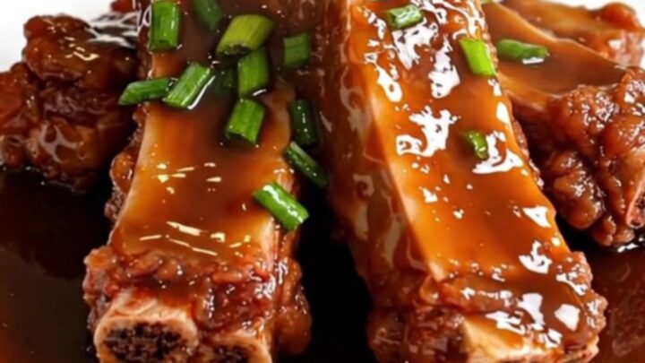 A close-up of tender, glazed boneless country-style pork ribs in a matte black slow cooker on a white quartz countertop.