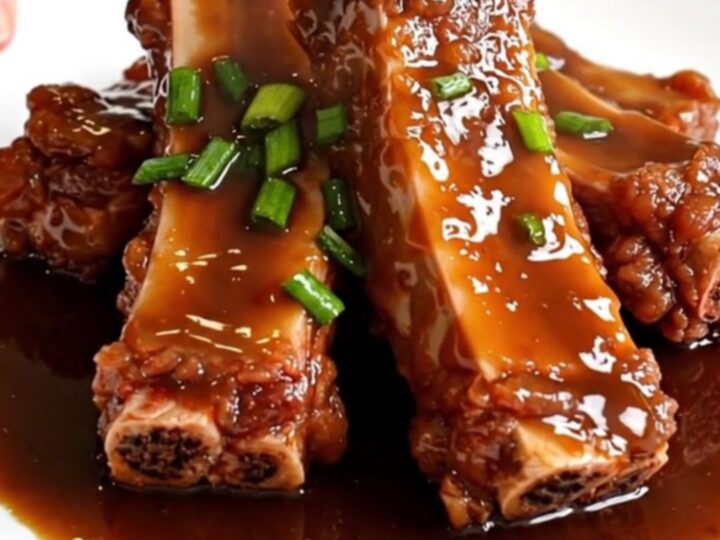 A close-up of tender, glazed boneless country-style pork ribs in a matte black slow cooker on a white quartz countertop.