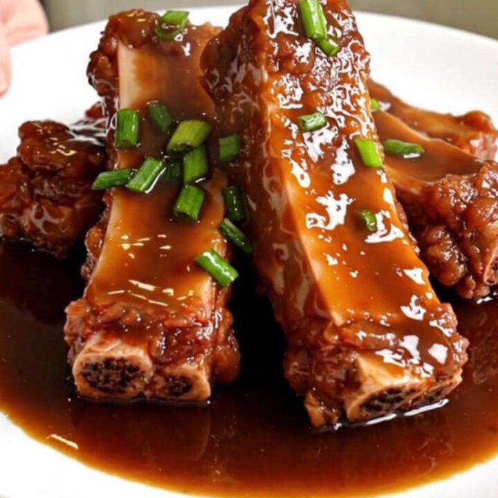 A close-up of tender, glazed boneless country-style pork ribs in a matte black slow cooker on a white quartz countertop.