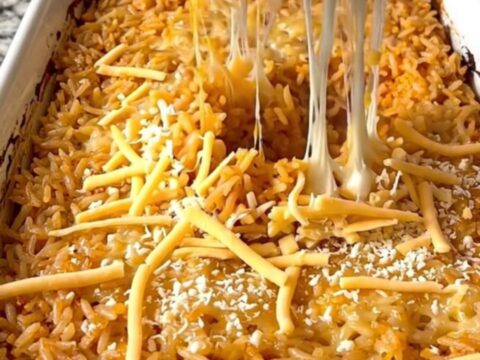 A rectangular ceramic baking dish filled with golden, cheesy Mexican rice on a granite countertop.