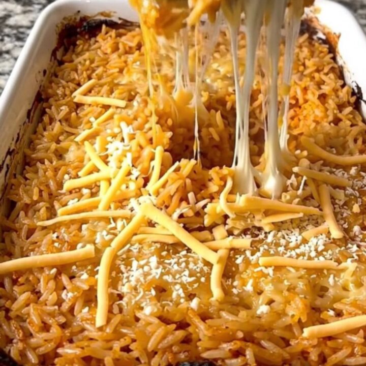 A rectangular ceramic baking dish filled with golden, cheesy Mexican rice on a granite countertop.