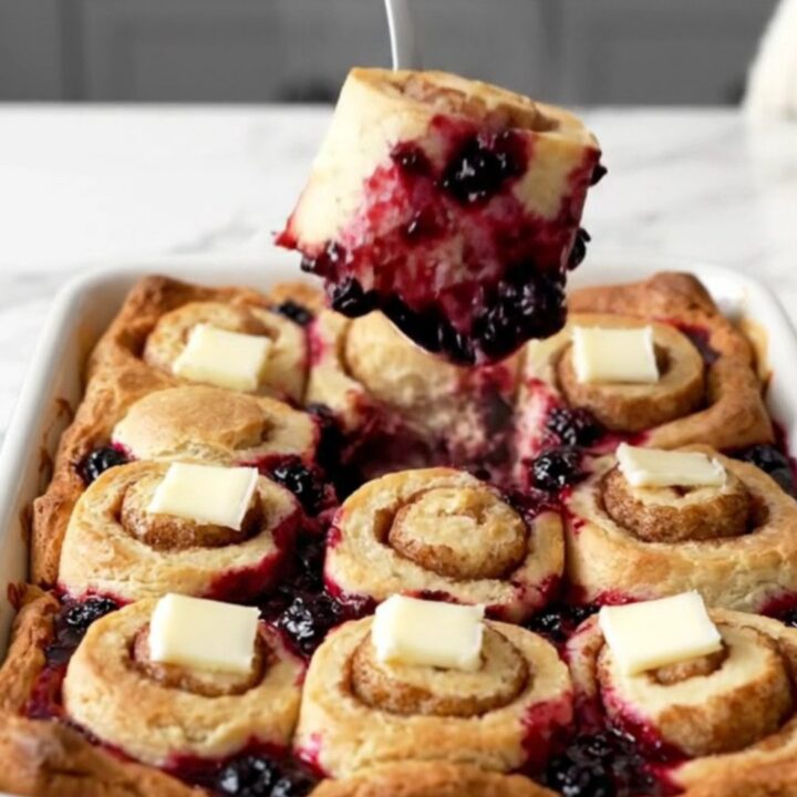 A large white ceramic dish filled with golden-brown cinnamon roll pieces and bubbling blueberry filling.