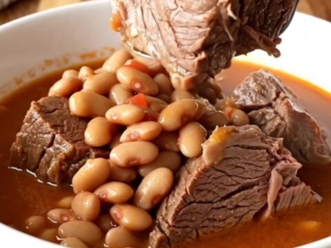 A rustic white bowl filled with tender chunks of slow-cooked chuck roast and pinto beans in a thick tomato broth.
