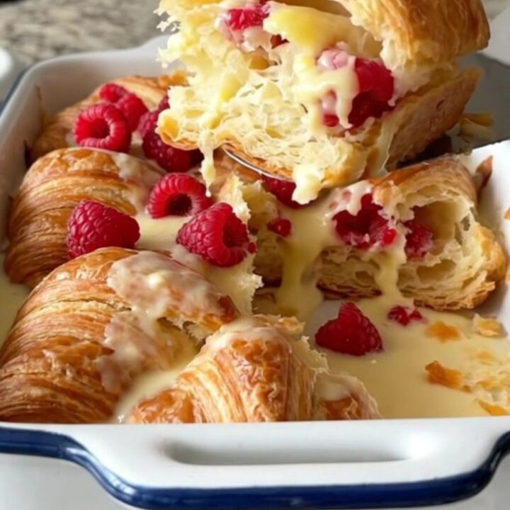 A golden, puffed raspberry cream cheese croissant bake in a white rectangular dish on a granite surface.