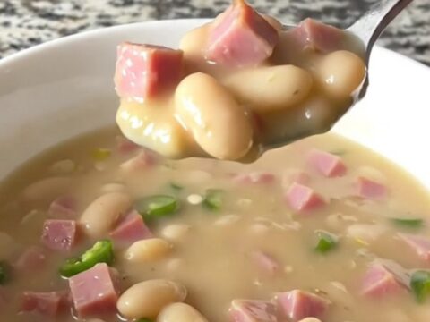 A white bowl filled with creamy white bean and ham chili, garnished with a few pieces of ham.