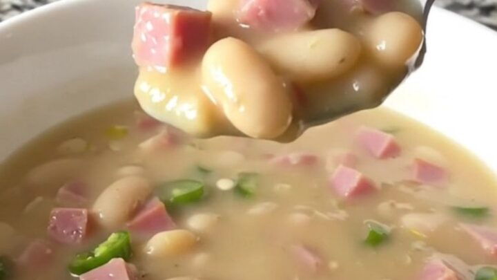 A white bowl filled with creamy white bean and ham chili, garnished with a few pieces of ham.