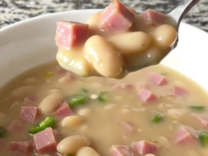 A white bowl filled with creamy white bean and ham chili, garnished with a few pieces of ham.