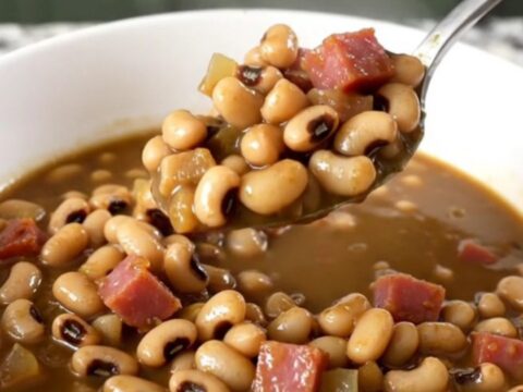 A white bowl filled with black-eyed peas, diced ham, and onion in a savory, thick broth.